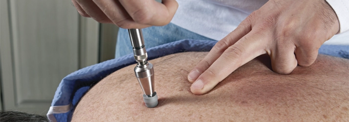 Chiropractor using an activator tool on a patient’s back for spinal adjustment