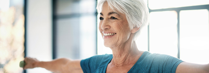 Smiling senior woman stretching her arms indoors, enjoying a moment of wellness.